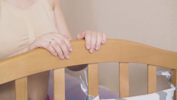 Young Mother Takes Care of Baby Rocking Wooden Crib in Room