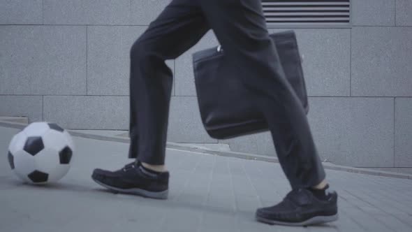 Feet of Well-dressed Boy Walking on the Street Leading the Ball and Holding Purse