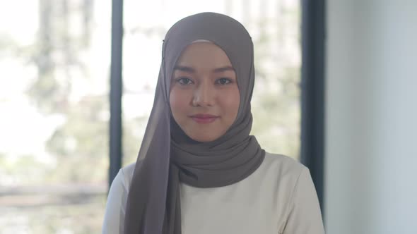 businesswoman looking at camera and smile, happy in workplace. Young Asian muslim lady stand relax.