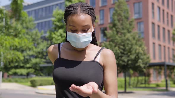 A Young Black Woman in a Face Mask Applies Disinfection Gel on Her Hands and Looks at the Camera