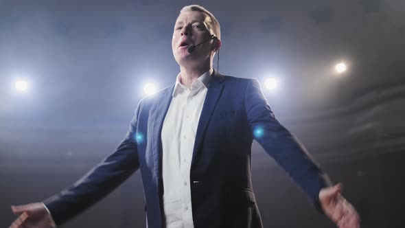 Portrait of Men Speaking Through a Microphone in Dark Conference Hall, Person Says About Marketing