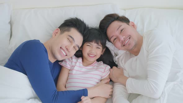 Asian handsome man gay lying down on bed with husband couple and kid daughter in bedroom at home.