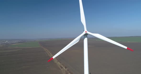 Close up flying footage of a rotating wind turbine in plowed fields with blue skies on background