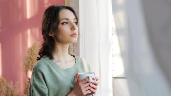 Beautiful Woman Sitting Near Window and Enjoy a Cupt of Tea Admiring Sunrise