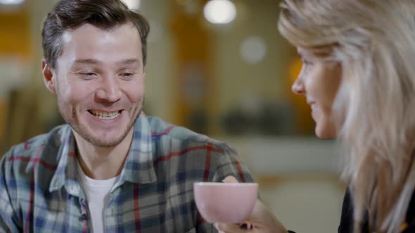 Handsome Young Man Is Chatting with Pretty Blonde Woman in a Cafe, He Is Joking and Amusing Her