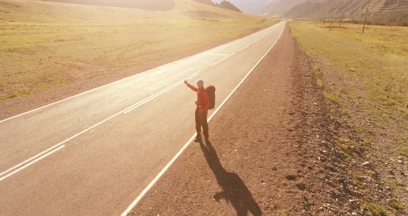 Flight Over Hitchhiker Tourist Walking on Asphalt Road. Huge Rural Valley at Summer Day. Backpack