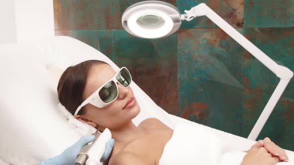 Woman Lying at Beauty Cliic in Protection Glasses and Having Laser Theraphy