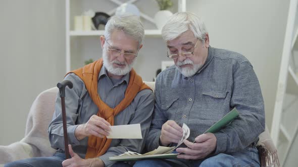 Portrait of Elderly Caucasian Men Watching Black and White Photos Indoors. Senior Male Retired