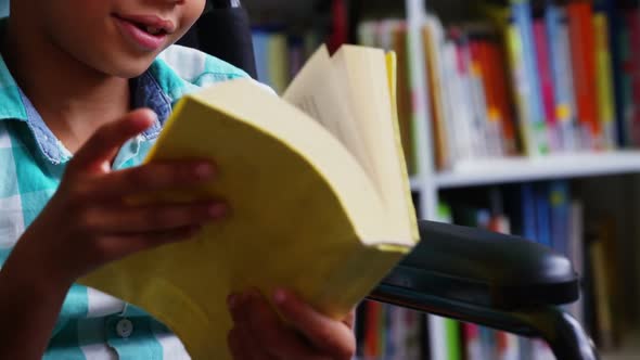 Disabled schoolboy reading book in library at school