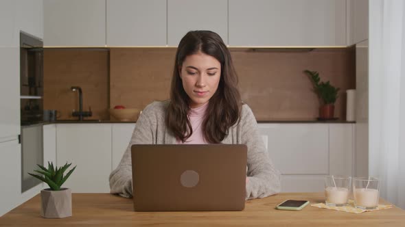 Pretty 20s Caucasian Woman Working on a Laptop on Her Kitchen Indoors