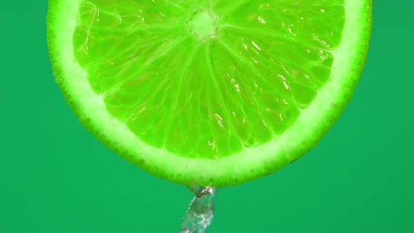 Water falling from green hue lime on green background. Orange slice and water splashing, drops