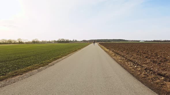 At a beautiful day, a sportive girl is inline skating along a rural road next to wide fields while t