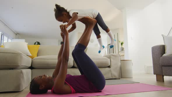 Happy african american mother and daughter doing yoga exercise at home