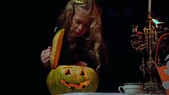 Halloween Pumpkin with Light Inside on Table in Night Forest with Blurred Little Girl Opening