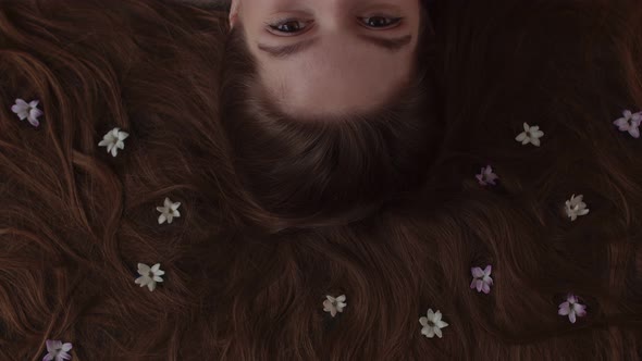 Blooming Flowers in the Hair of a Brunette Lying on Her Back Top View
