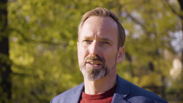 A Middleaged Handsome Caucasian Man Talks to the Camera with a Smile in a Park in Fall  Closeup