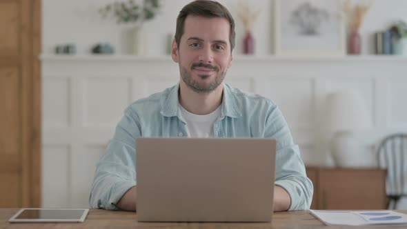 Young Man Smiling at Camera While Using Laptop