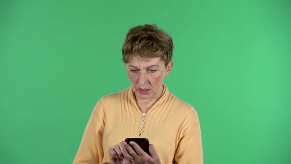 Portrait of Elderly Woman Is Texting on Her Phone Isolated Over Green Background.