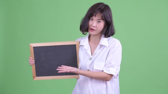 Stressed Asian Businesswoman Holding Blackboard and Giving Thumbs Down