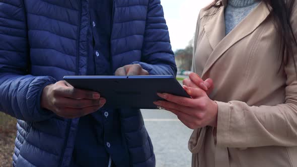 A Black Man and an Asian Woman Stand in a Street in an Urban Area and Work on a Tablet - Closeup