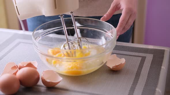 Female Hands Stirring Dough with a Mixer for Cake in a Bowl on a Table