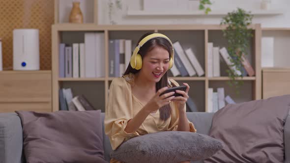 Young woman wearing yellow  headphones playing cell phone game. Female win the game in hard match, l