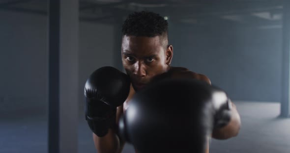 African american man wearing boxing gloves training throwing punches in empty room