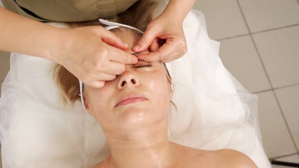 Cosmetologist in Green Coat Massages Mature Woman Eyebrow