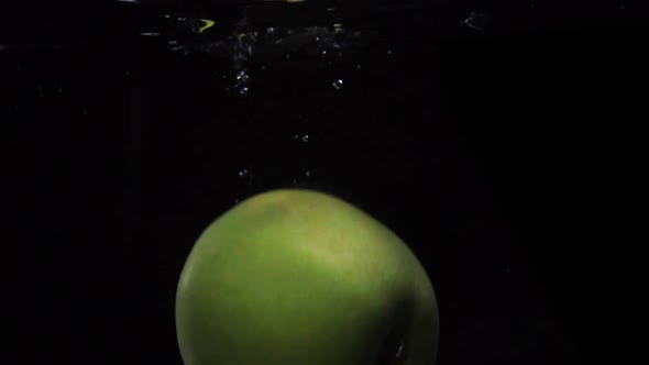 Slow Motion Shot: Green Apple Falls and Floats in Water. Black Background. Food Video Apple