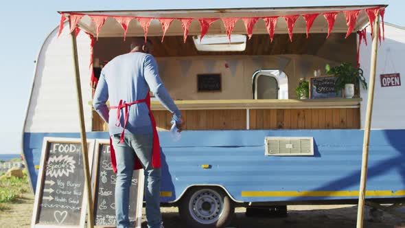 Rear view of african american man wearing apron smiling while cleaning the food truck