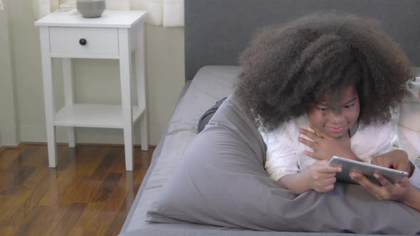 Happy young African mother using tablet computer with daughter for education and learning on bed.