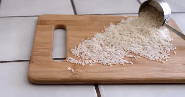 A pile of white rice grains pouring from a measuring cup in a kitchen for a plant based recipe SLIDE