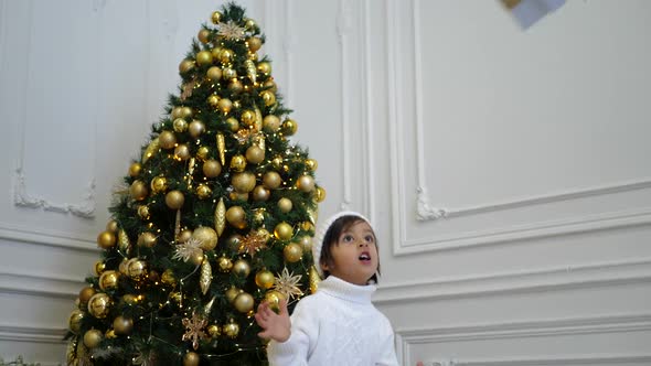 Portrait of a Boy a Child in a White Knitted Sweater and Hat Stands at the Christmas Tree