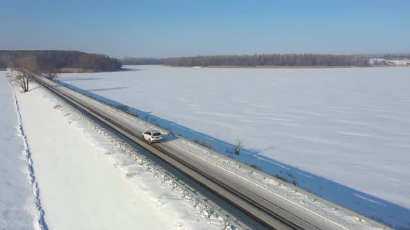 Aerial Shot of Car Riding Through Snow Covered Road Near Frozen Lake