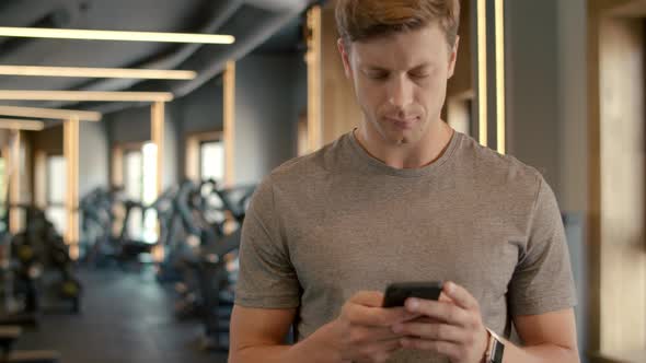 Handsome Sportsman Texting Message in Sport Club. Bodybuilder Standing at Gym alt
