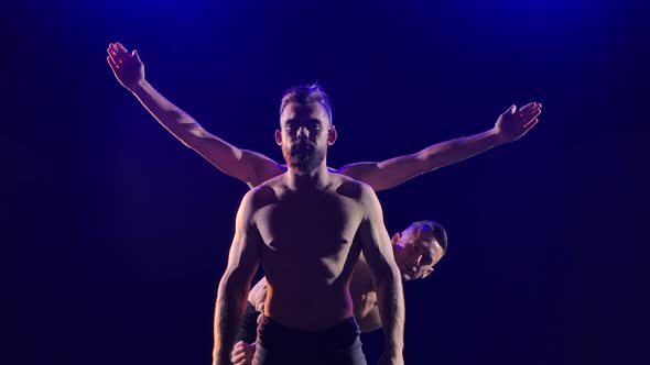 Group of Acrobatic Gymnasts Perform Acrobatic Exercises. Shot in a Dark Studio with Blue Light. Slow