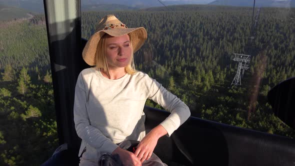 A Young Beautiful Woman Sits in a Cable Car and Looks Over the Landscape Below with a Smile