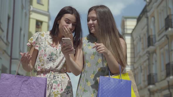 Two Happy Girlfriends After Shopping with Shopping Bags in Front of Beautiful Buildings Discussing