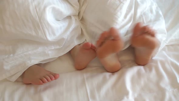 Close-up of Mom's Feet and a Small Child Under a White Blanket on the Bed.