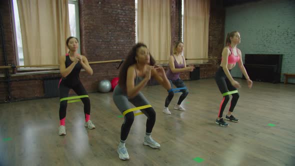 Sporty Fit Females Practicing Banded Squats Indoor