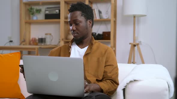 Man Talking on Phone and Using Laptop on Couch in Home Room Spbas