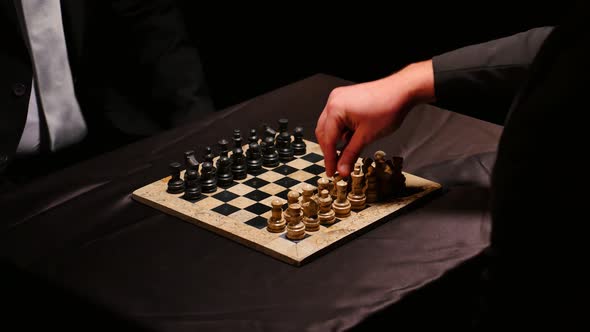 Footage of two men in suits playing chess in a dark room, the game just started