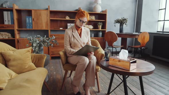 Redhead Female Psychologist Taking Notes and Posing for Camera at Work