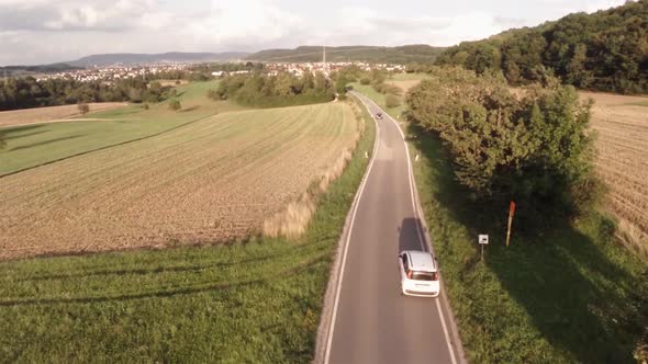 Aerial view of an small road in Germany. A white car drives on the road. Wide shot. Small city in th