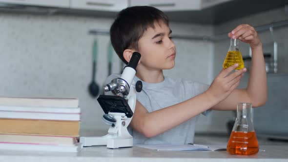 Close-up. The Boy Teaches Chemistry Using a Microscope and Flasks with Liquid and Makes Notes in a