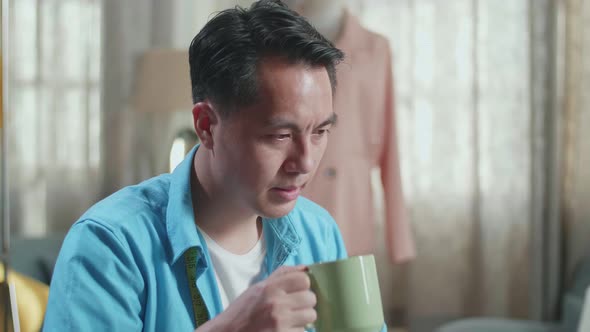 Close Up Of Asian Male Designer Working On A Laptop And Drinking Coffee While Designing Clothes