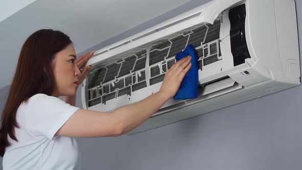 young woman cleaning the air conditioner with cloth at home