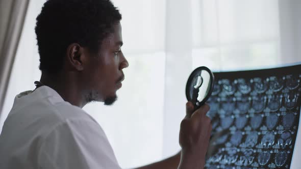 Closeup Focused Male Doctor Standing at Window Analyzing Xray with Magnifying Glass