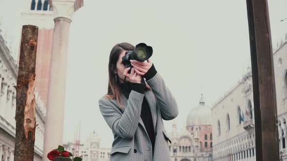 Beautiful Female Professional Photographer with Camera Taking Photos Near Wooden Pillars in Old Town