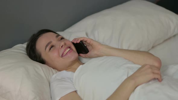 Young Woman Talking on Smartphone Laying in Bed